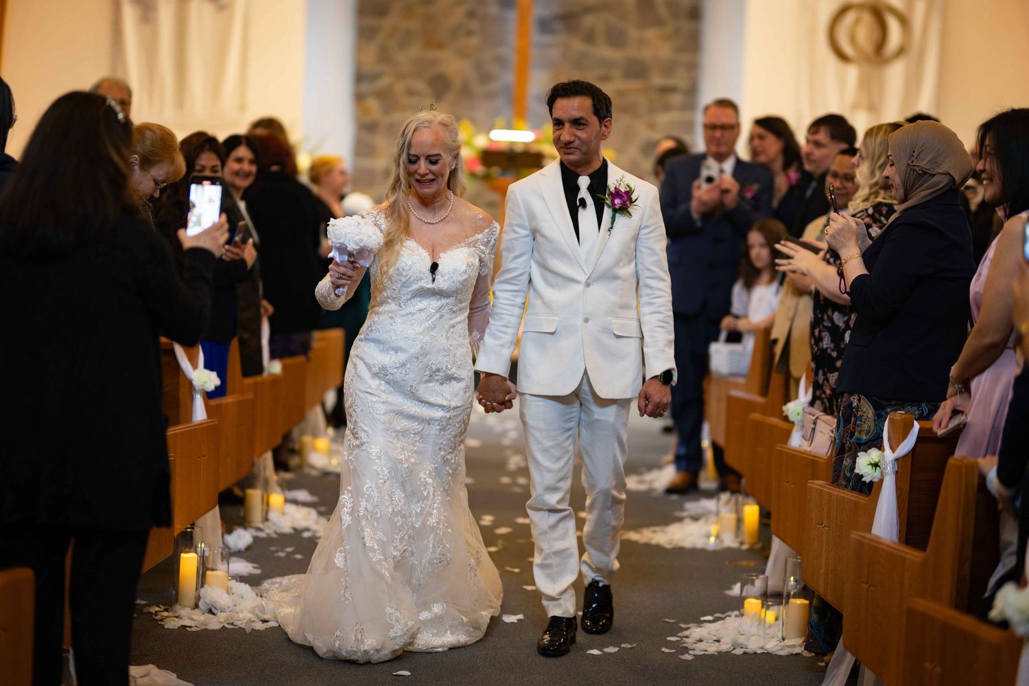 A bride and groom walk down the church aisle together while wedding guests look on from the pews.