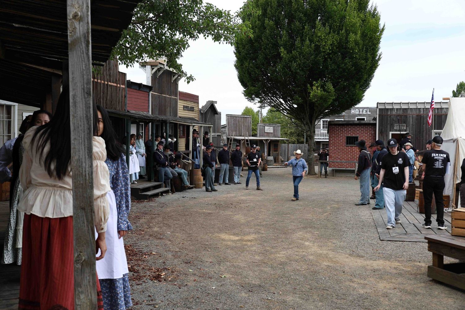 Visitors explore a historic western town boardwalk with wooden buildings and storefronts.