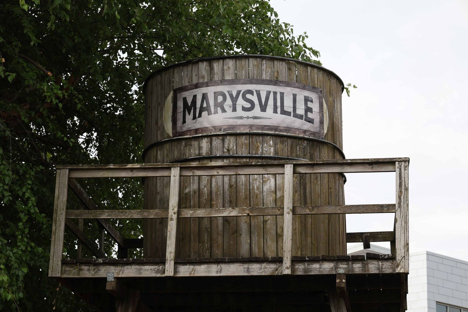 Weathered wooden water tower with 'Marysville' text stands against a cloudy sky.