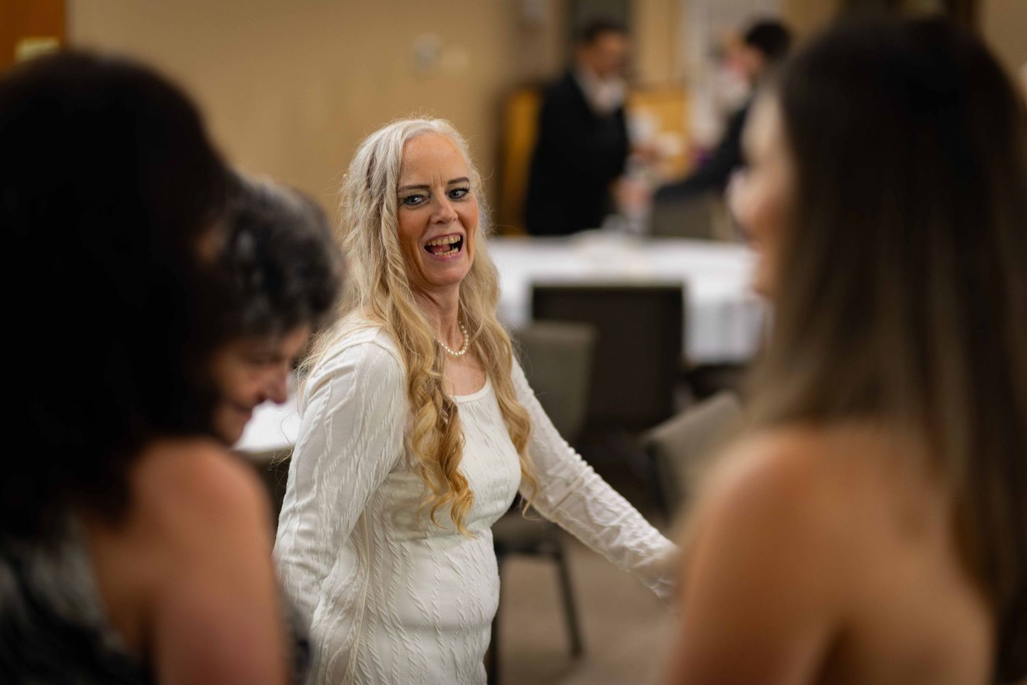 A bride in a white dress laughs joyfully during a wedding reception celebration.