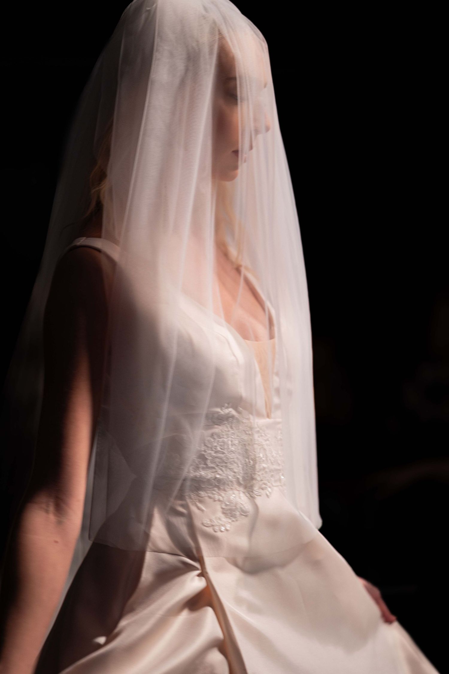 A bride in a white wedding dress and veil is shown in a dramatic silhouette against a dark background.