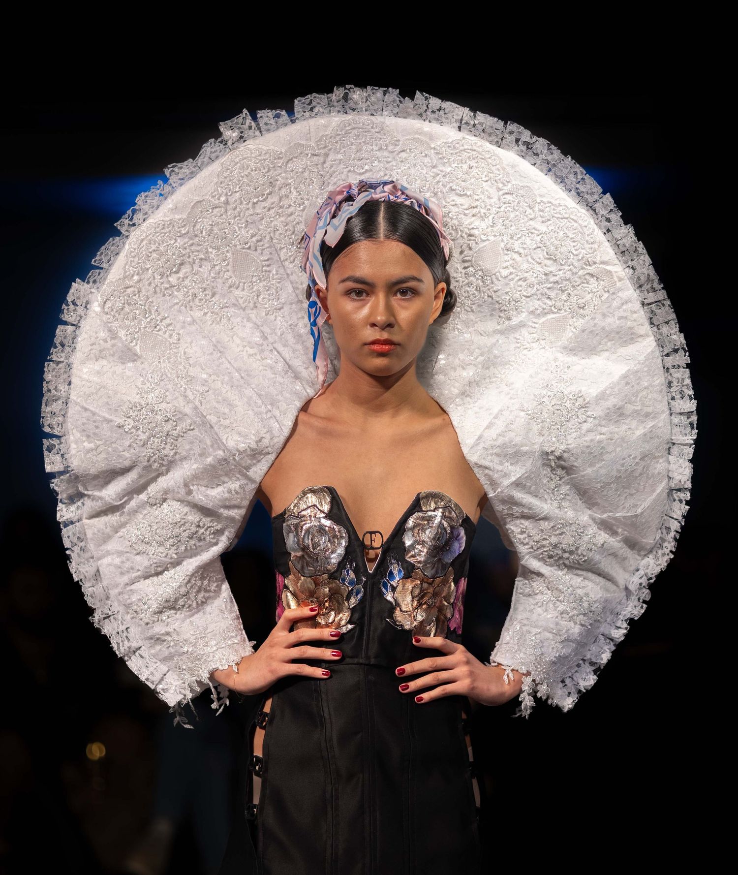 Fashion model walks runway in dramatic black gown with oversized white ruffled collar detail at fashion show.
