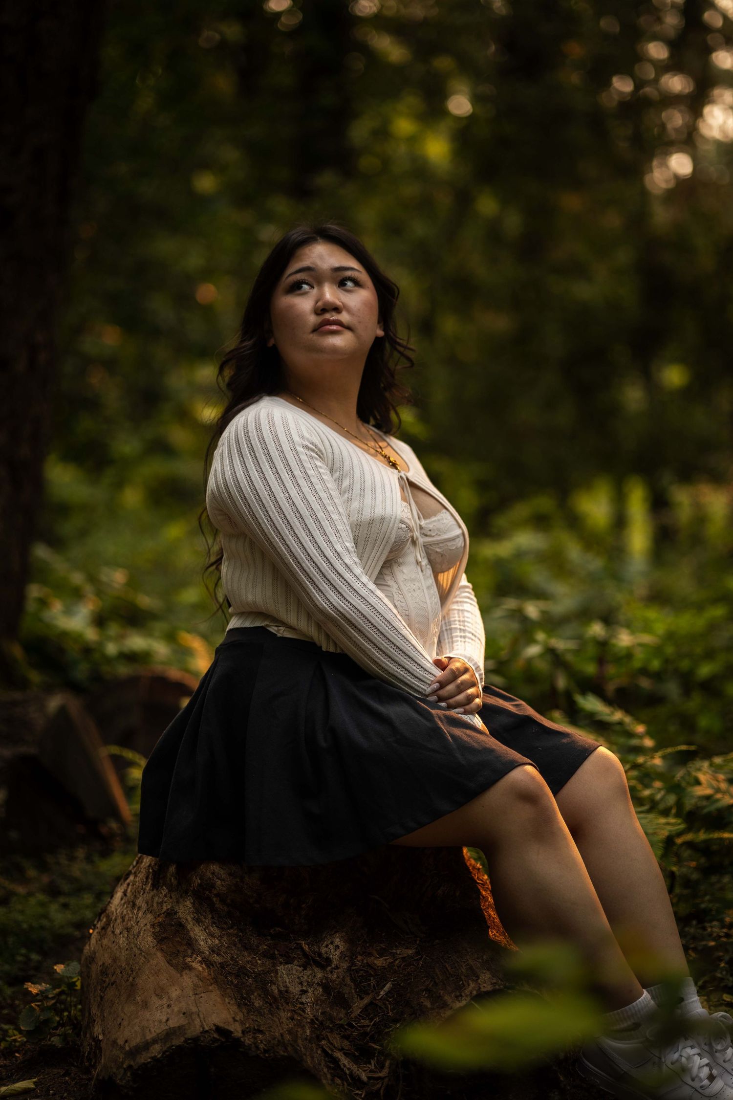Person in white sweater sitting on tree stump in autumn forest.