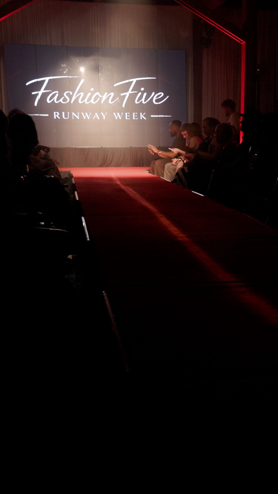 Fashion Five Runway Week event with red carpet catwalk, dimly lit venue, and seated audience judges panel.