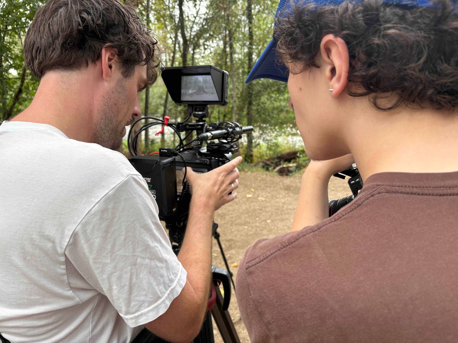 Behind the scenes footage being filmed outdoors with camera operators and crew members in a wooded setting.