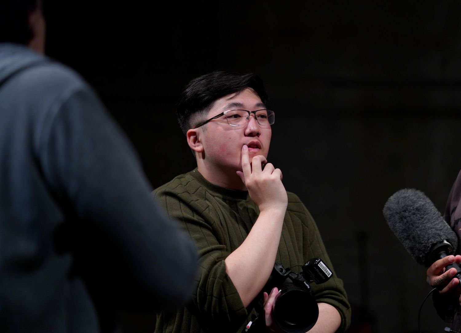 Person in black clothing speaking into microphone against dark background.