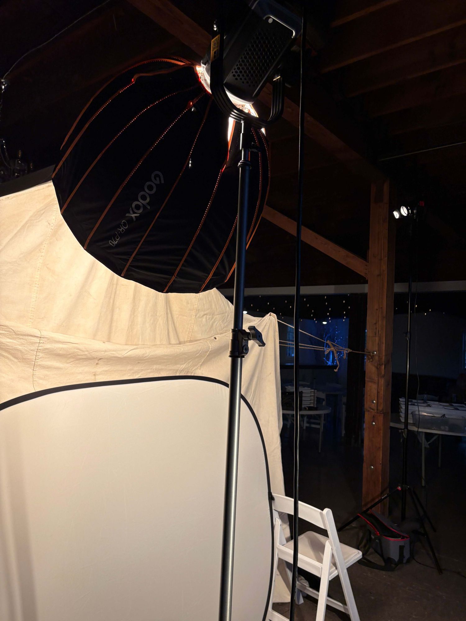 Photography studio setup with lighting equipment and white backdrop against dark wooden beams in an attic space.