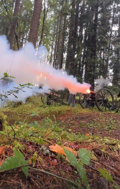 Civil War reenactment with cannons firing smoke in a forest setting.