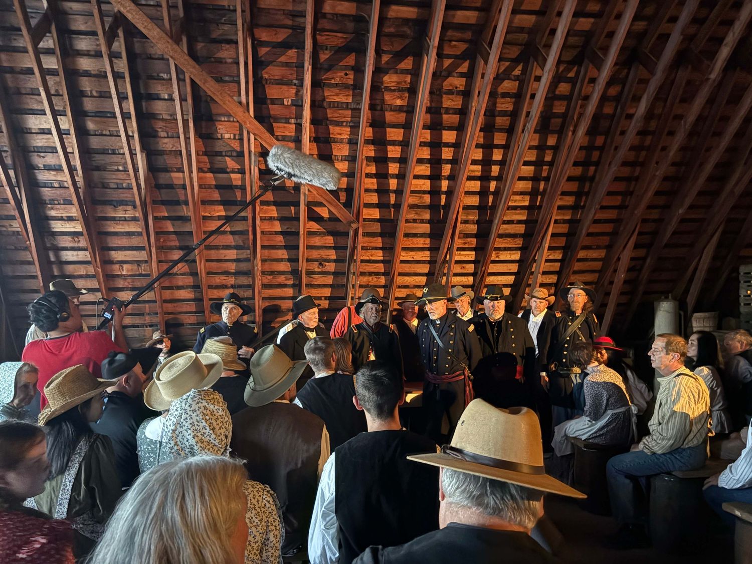 A group of people gather inside a rustic wooden barn attic space for a meeting or presentation.