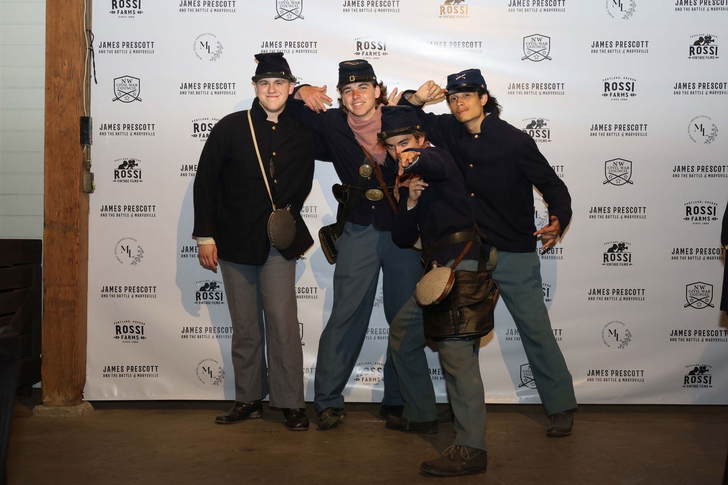 A group of friends pose playfully in front of a branded photo backdrop at an event.