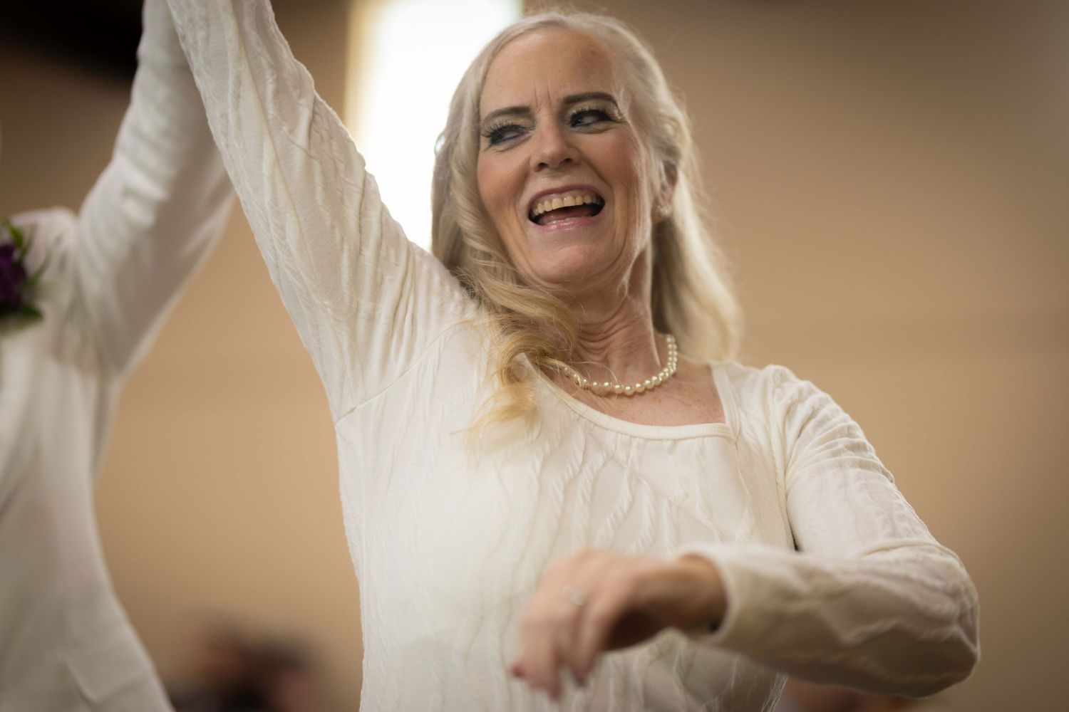 A joyful bride in a white wedding dress laughs and dances during a celebration.