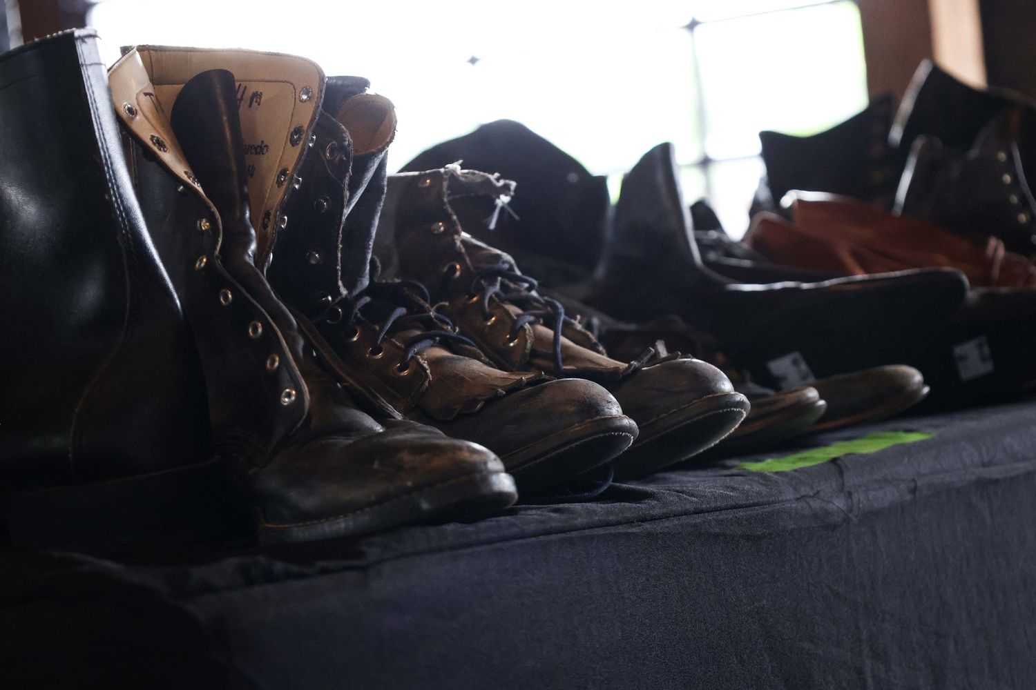 A row of black combat boots and shoes lined up on a dark surface, showing different styles and wear patterns.