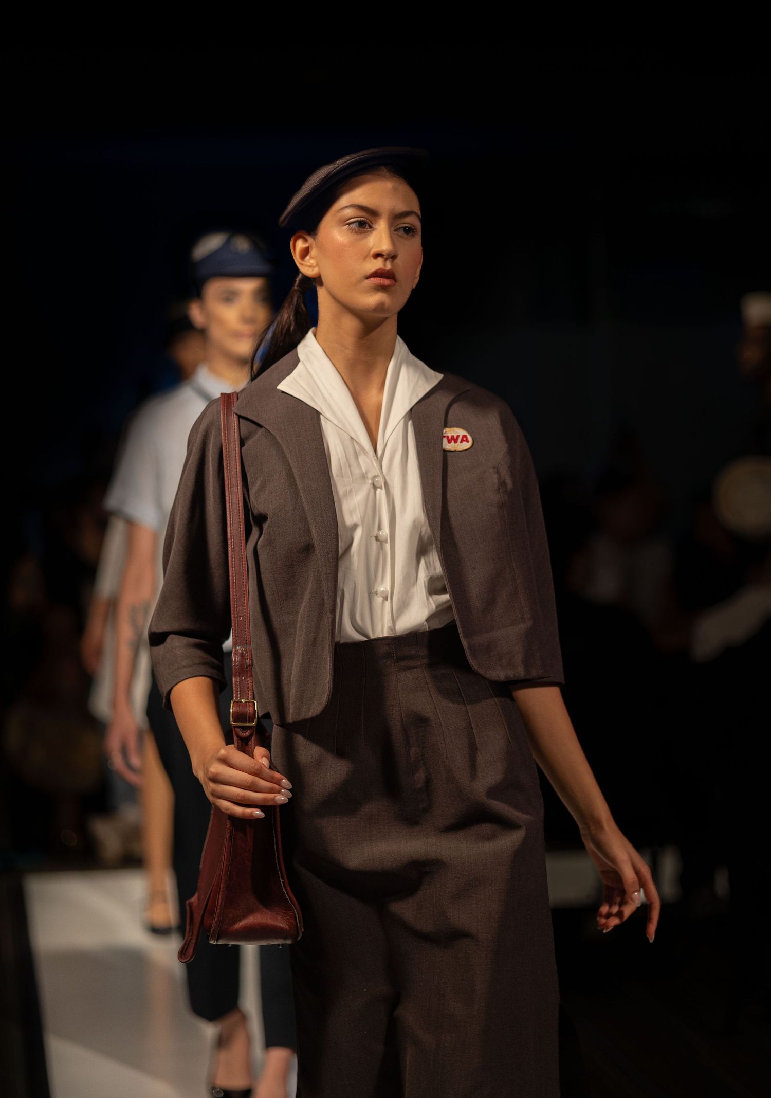 Models walking runway in vintage-style brown suits and white blouses.