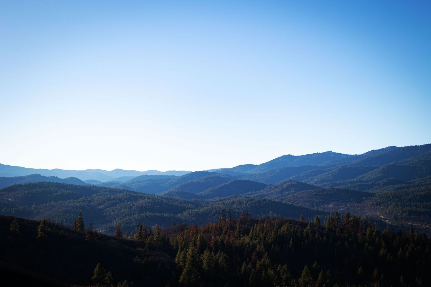 A panoramic view of rolling mountain ranges stretches across the horizon under a bright blue sky.