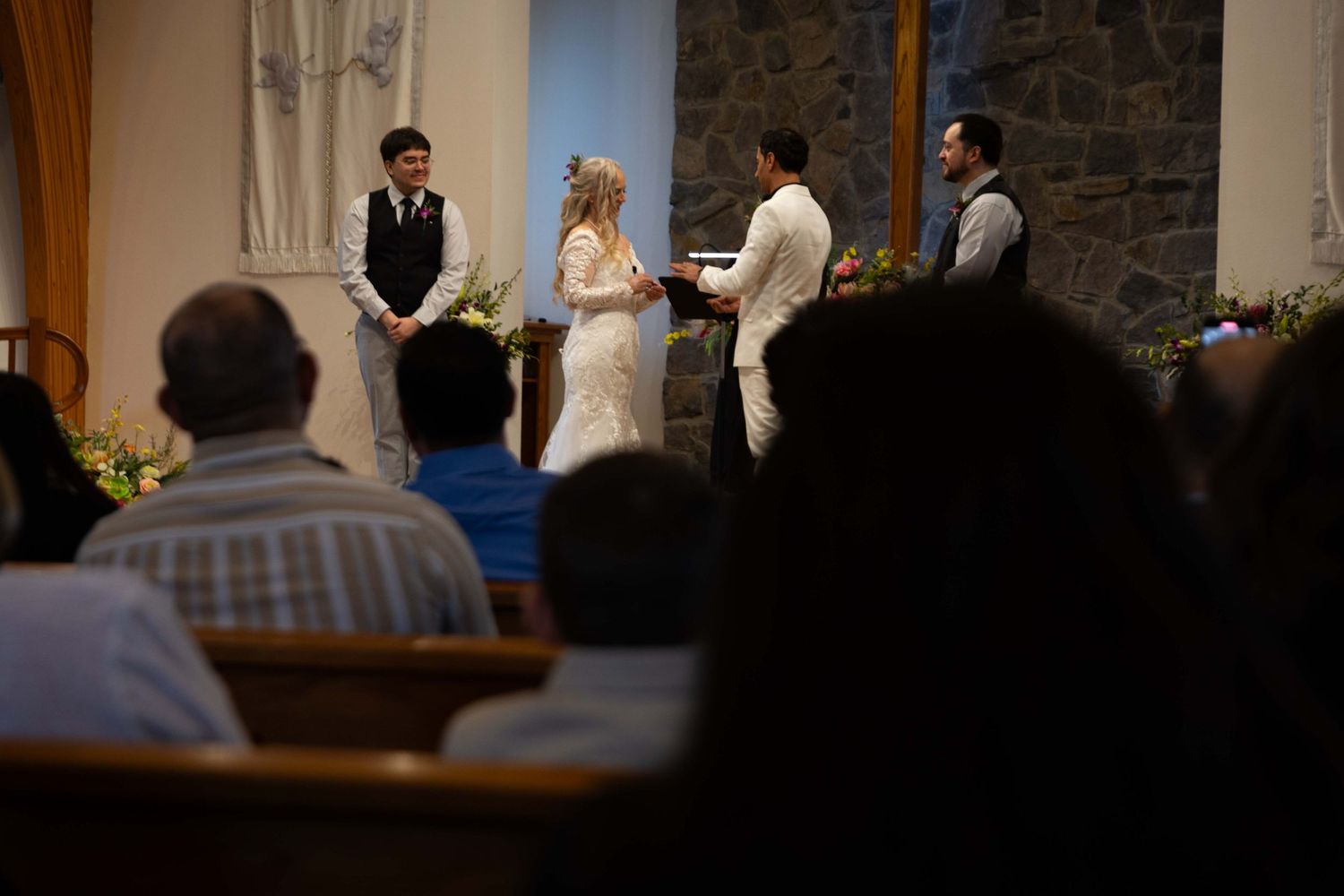 Wedding ceremony taking place in a church sanctuary with stone walls and wooden pews.