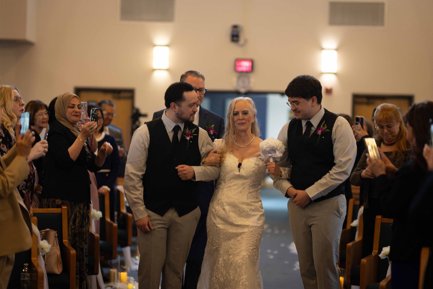 Wedding guests dancing and celebrating in a reception hall with warm lighting and festive atmosphere.