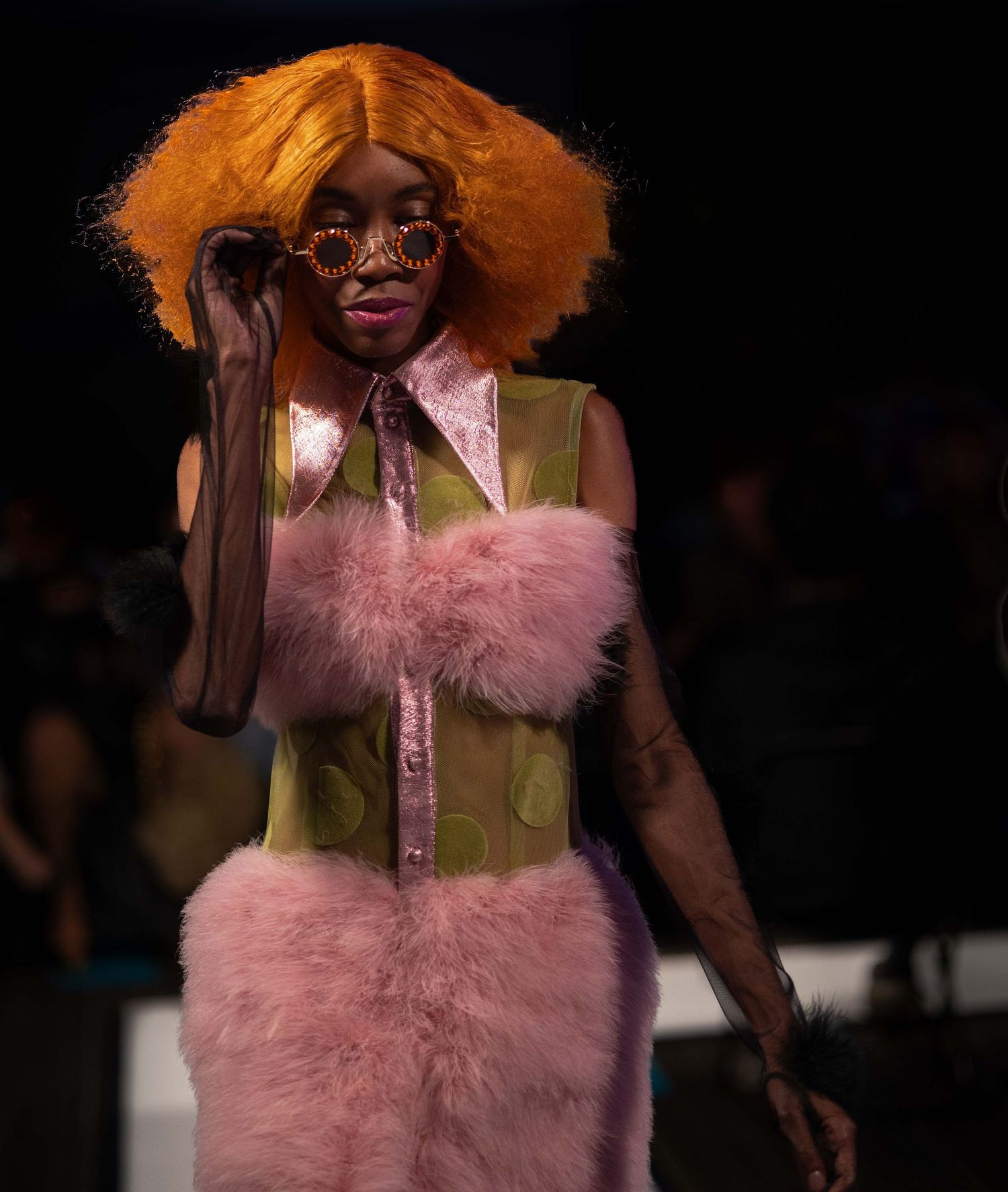 Fashion model wearing pink fur vest and olive green outfit on runway.