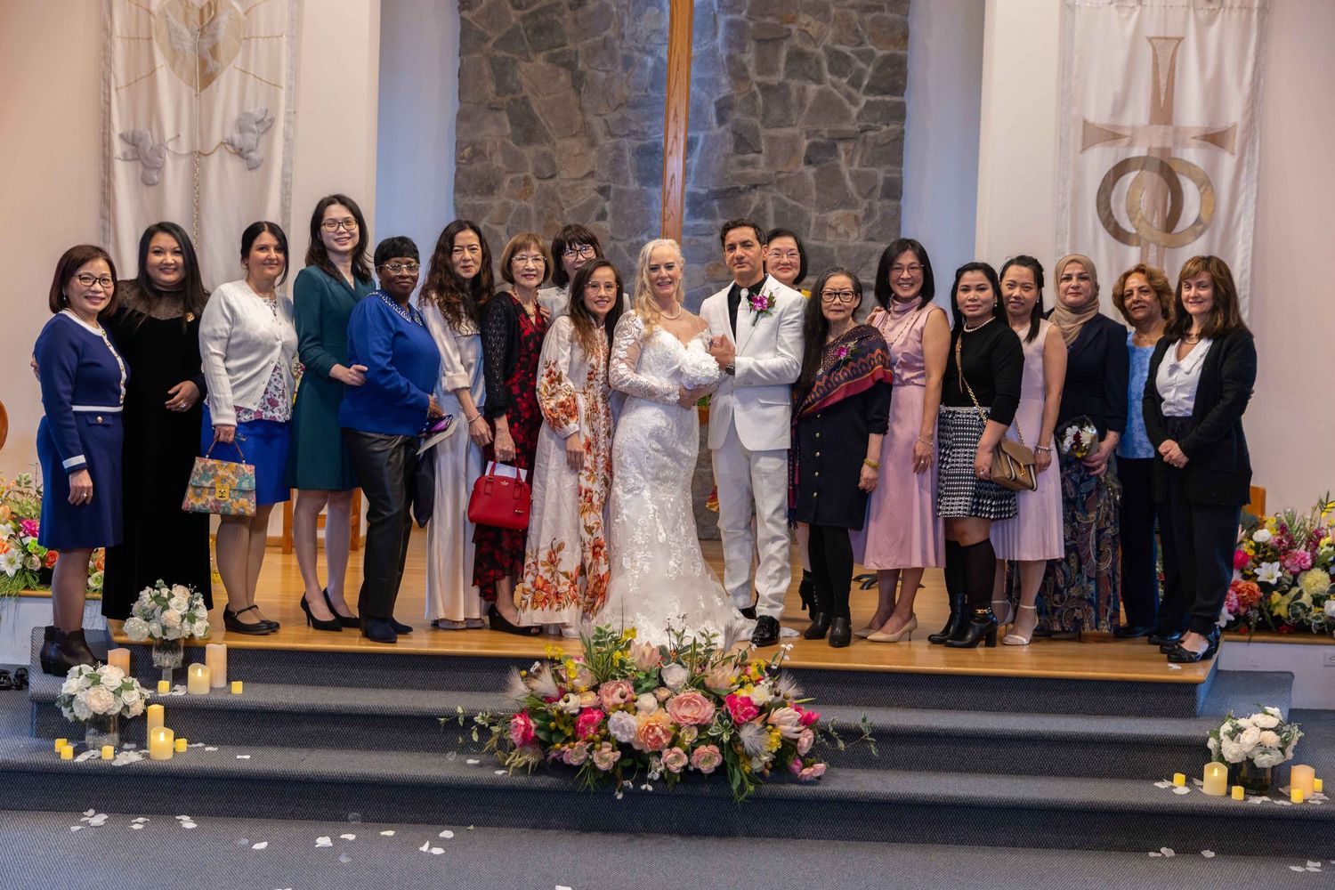 Group photo of wedding guests posing together in front of a stone wall at a church reception.