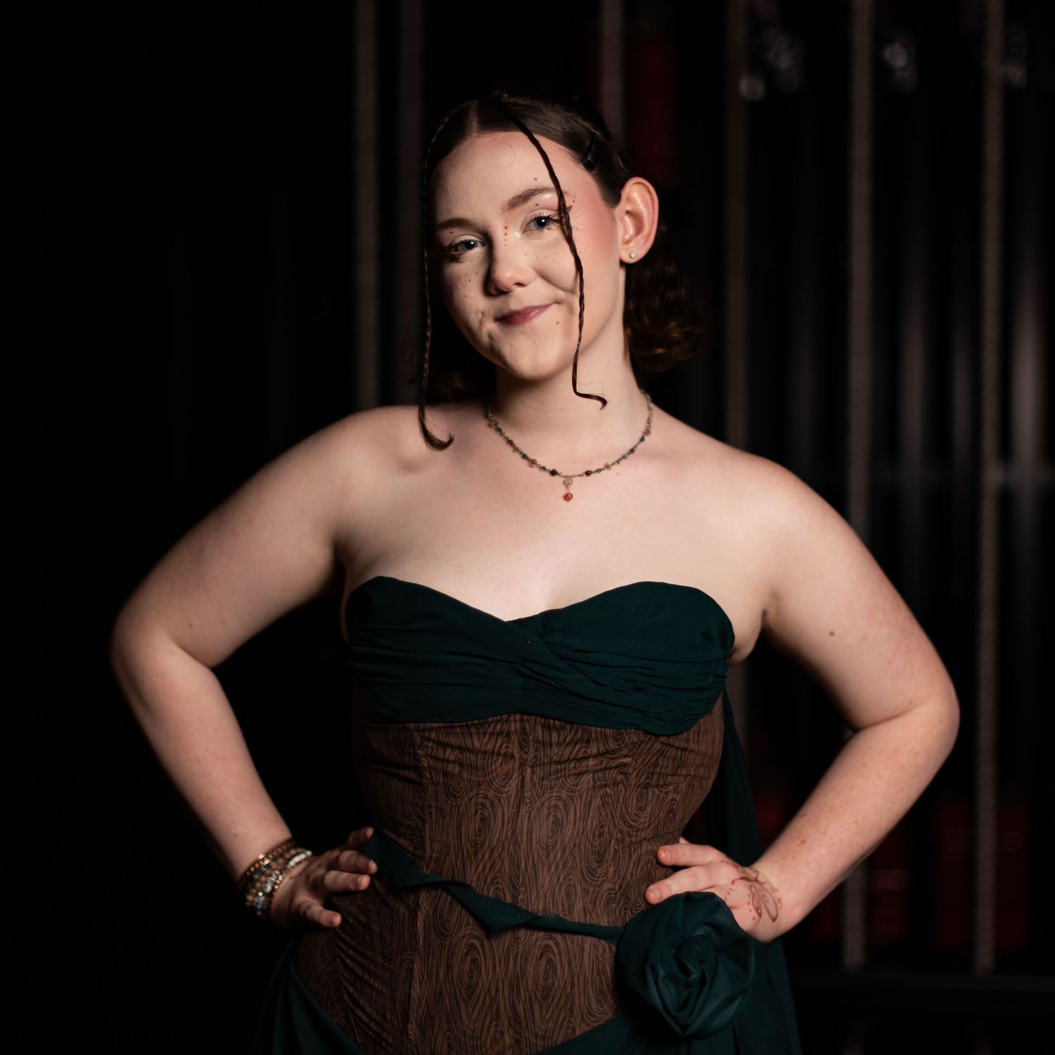 Person in dark corset poses against black background in dramatic lighting and elegant styling.