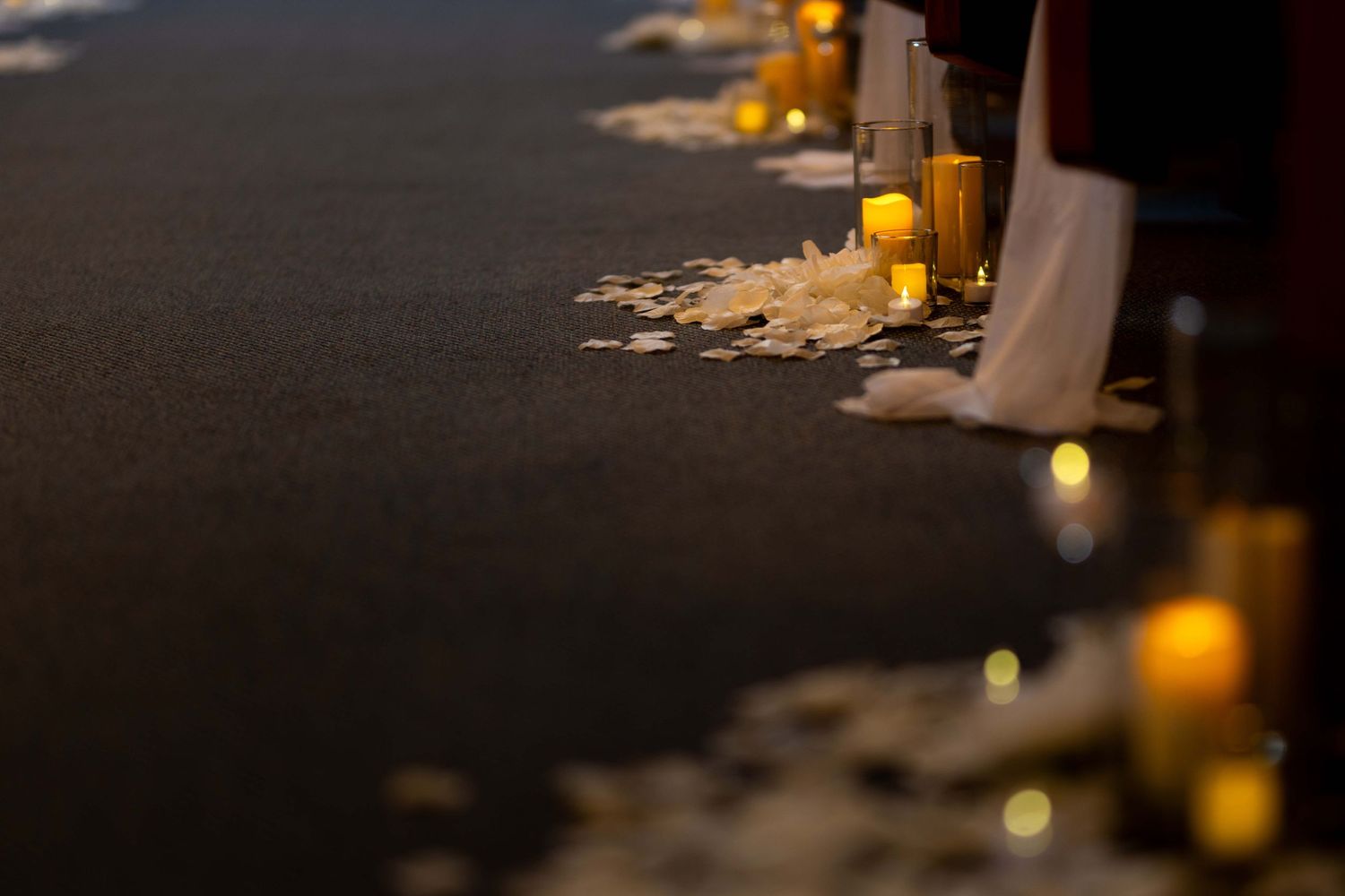 Candlelit aisle decorated with rose petals creates romantic ambiance at evening wedding ceremony.