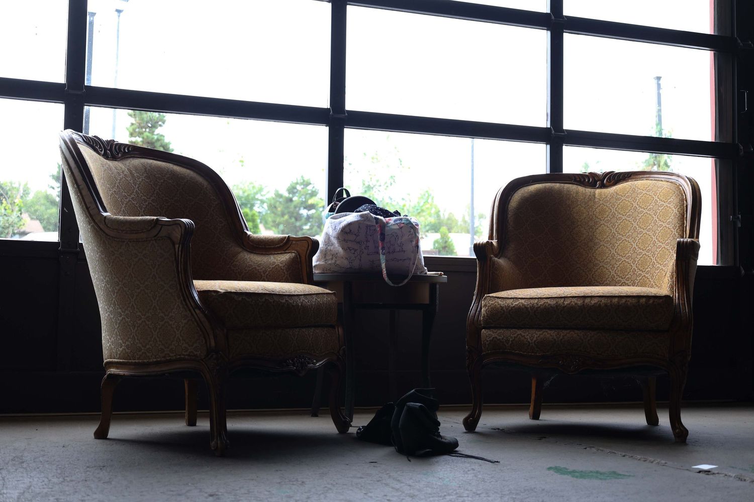 Two vintage armchairs in a dimly lit room with large windows creating a moody atmosphere.