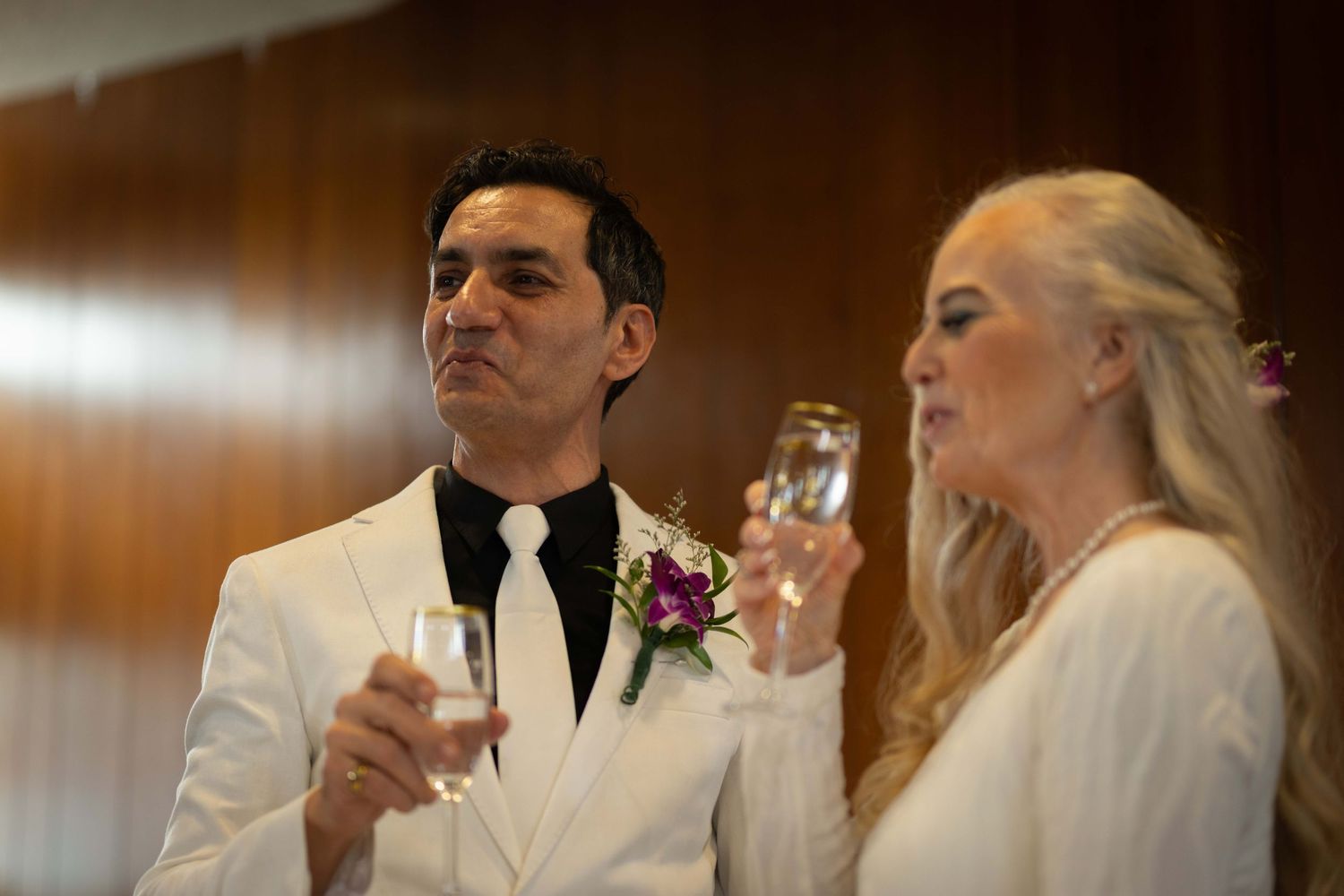 Wedding couple dressed in white sharing a toast during their reception celebration.