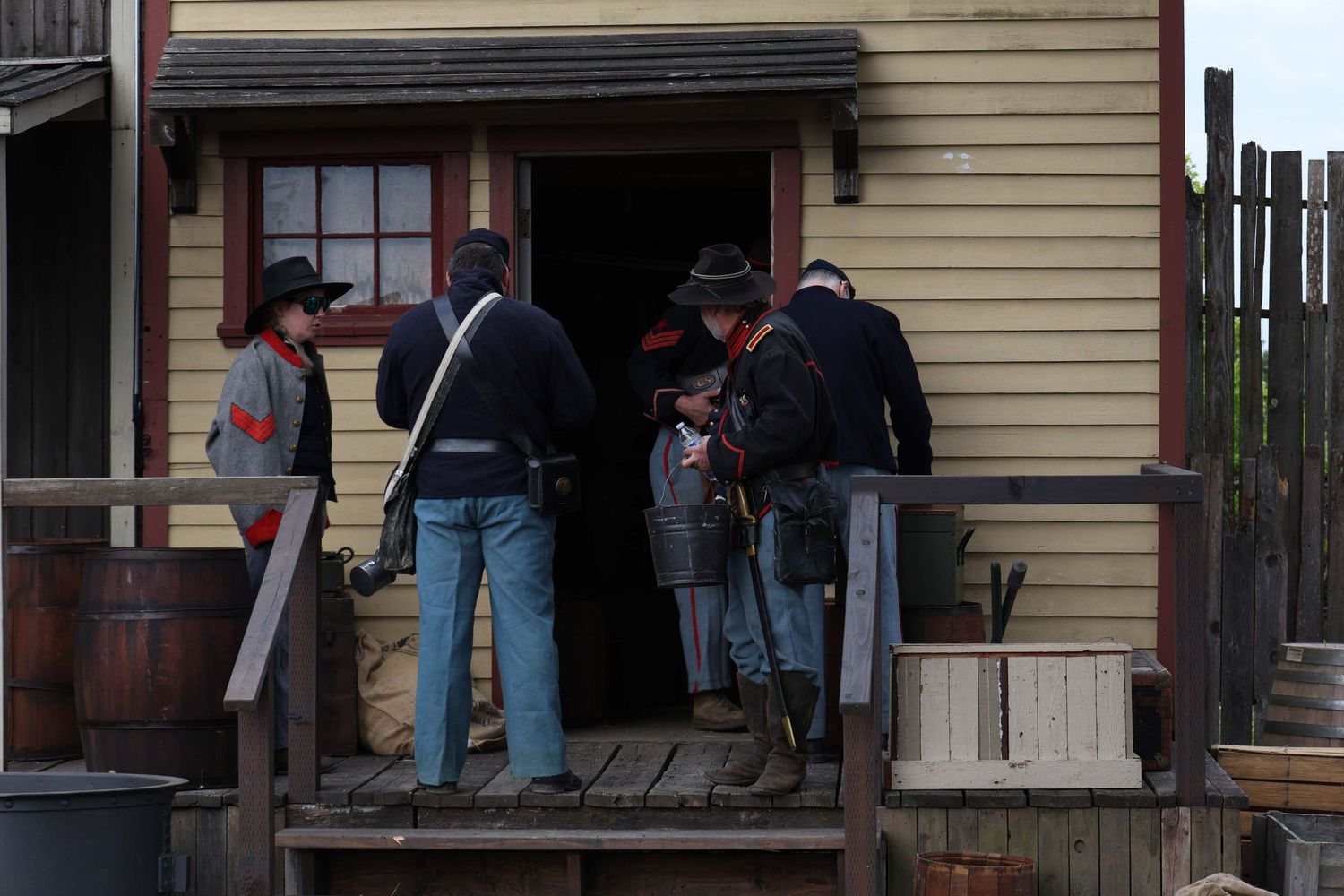 Wooden storefront porch of a historic building with people gathering outside.