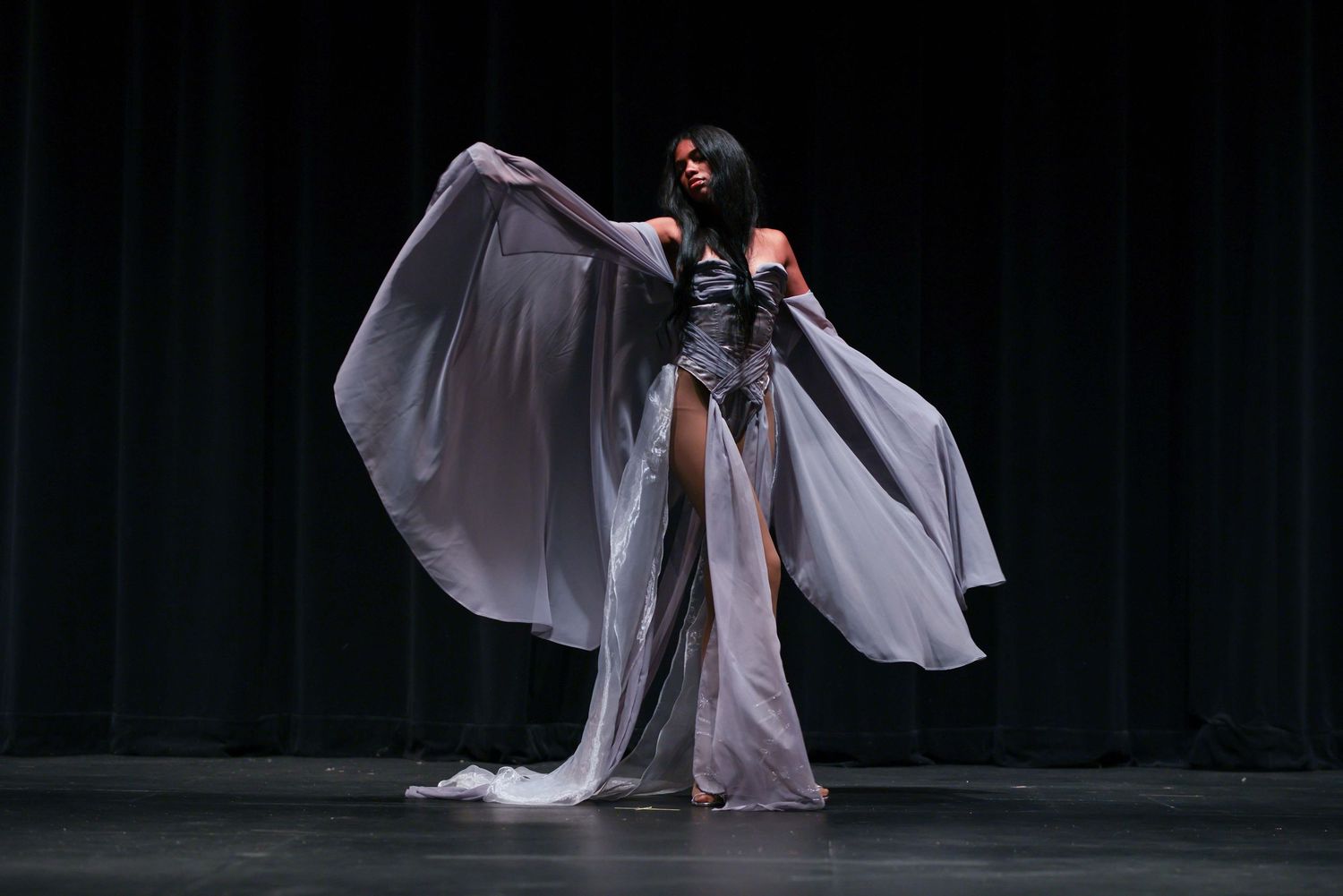 Dancers in flowing white costumes perform an ethereal contemporary dance piece on a dark stage.