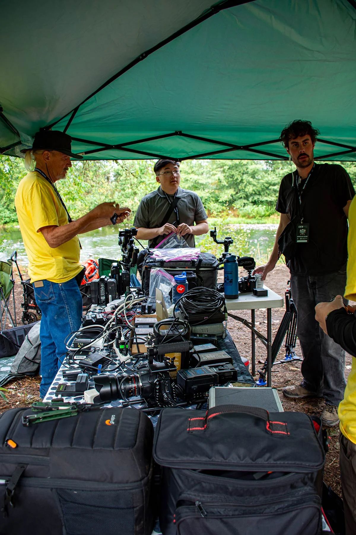 Camera operators set up professional video equipment under a green canopy tent at an outdoor event.