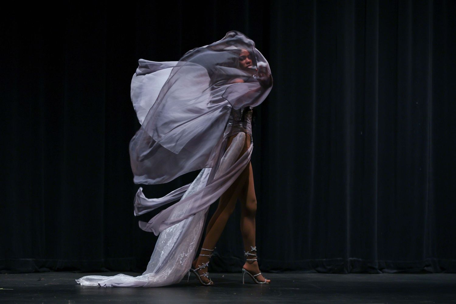 A ballet dancer in a flowing pink dress performs a graceful movement against a dark background.