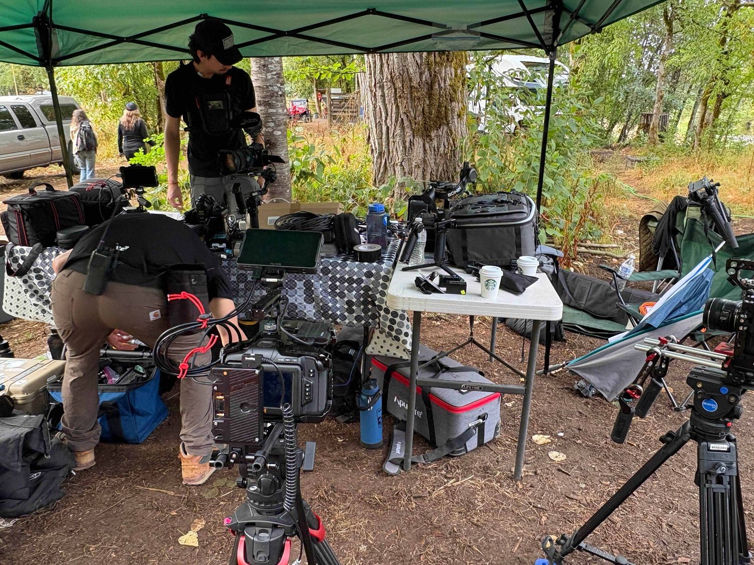 A series of outdoor encampments with tents and makeshift shelters set up under trees and canopies.