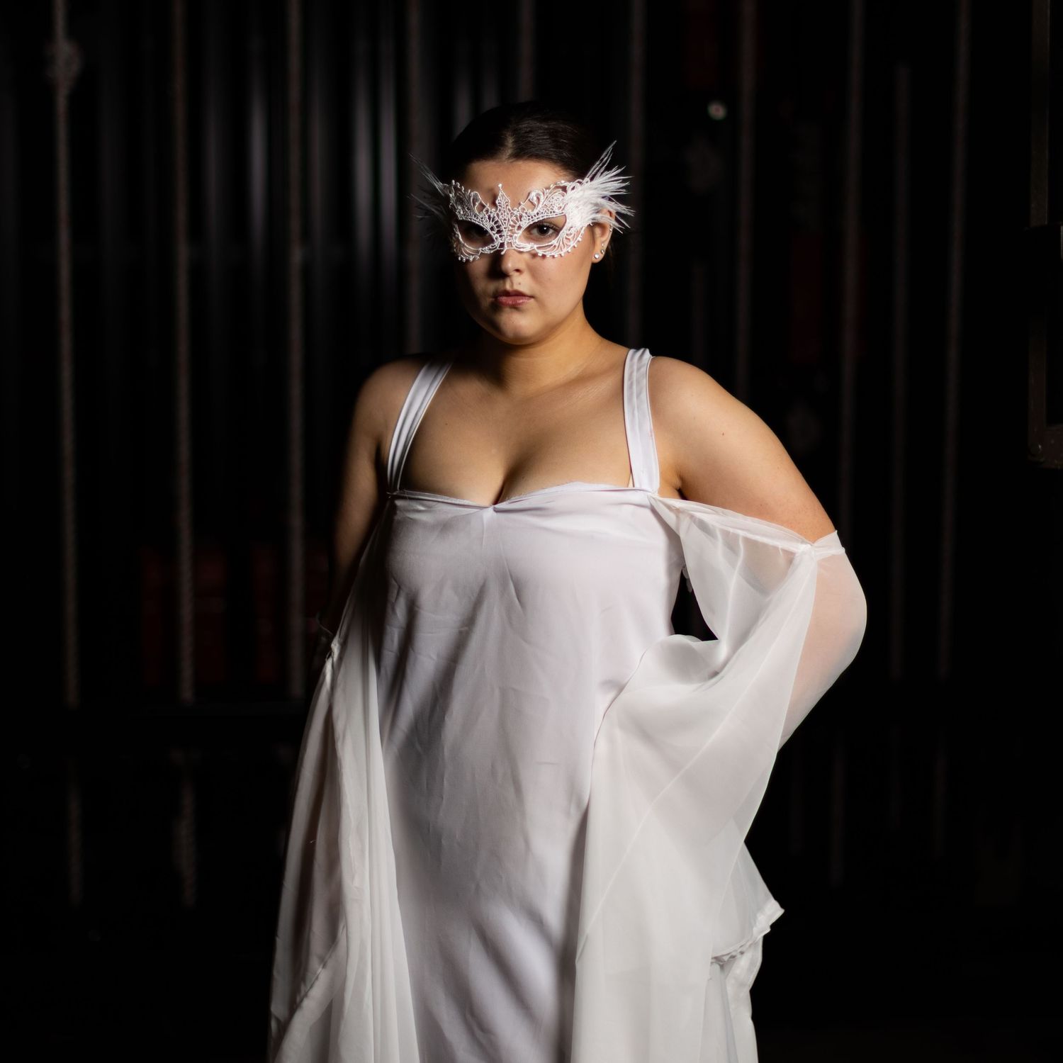 Person in white clothing and lace mask poses against dark background in artistic portrait series.