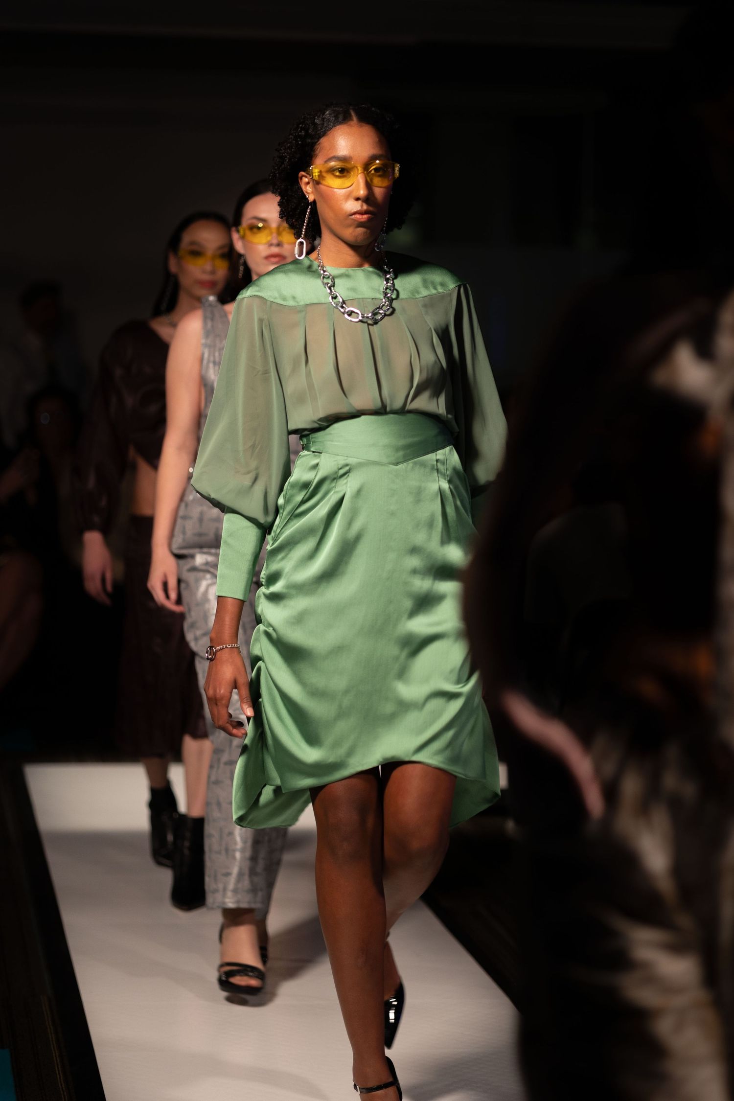 Models walk the runway in mint green satin dresses during a fashion show presentation.