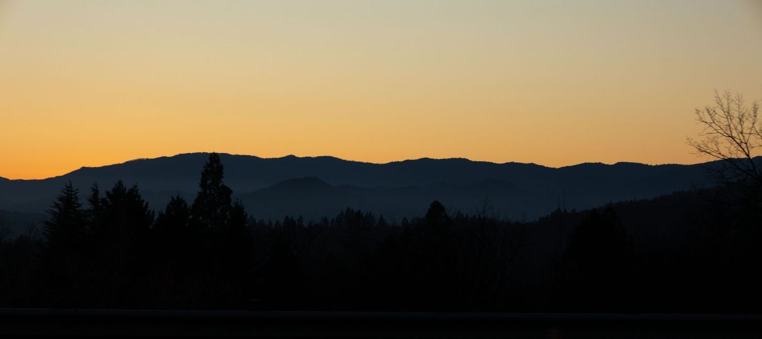 Silhouetted mountain range and forest treeline against an orange sunset sky.
