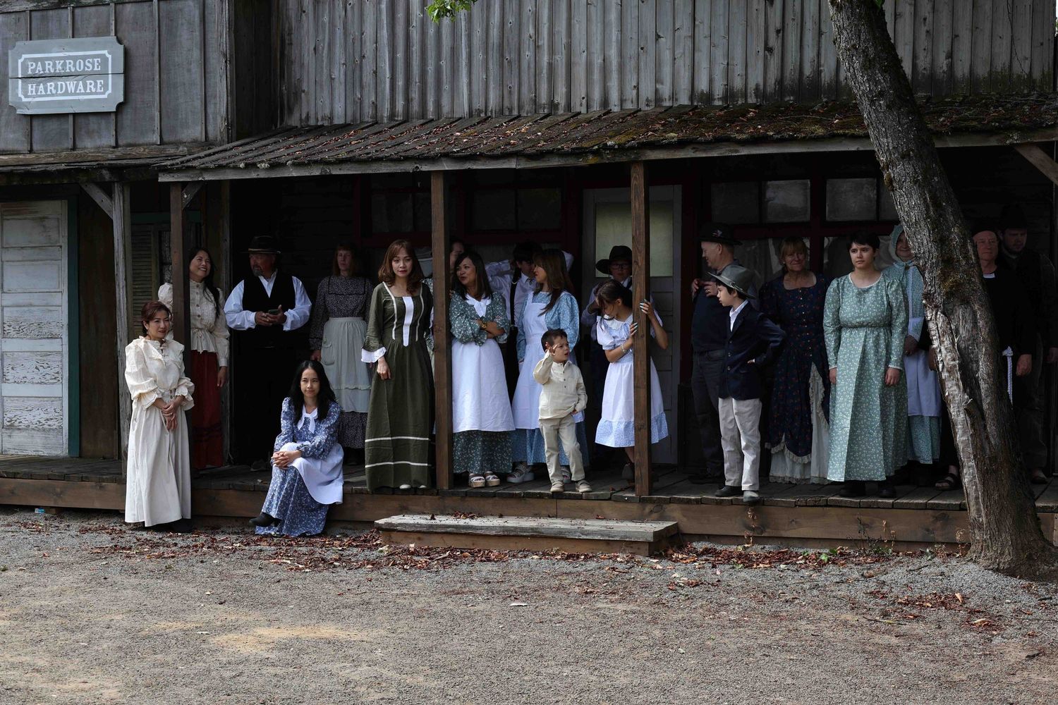 Historical reenactors in period clothing gather on a wooden porch at a living history museum.