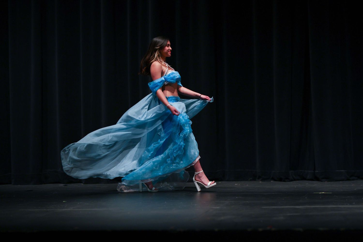 A ballet dancer in a flowing blue dress performs an elegant leap on a dark stage.