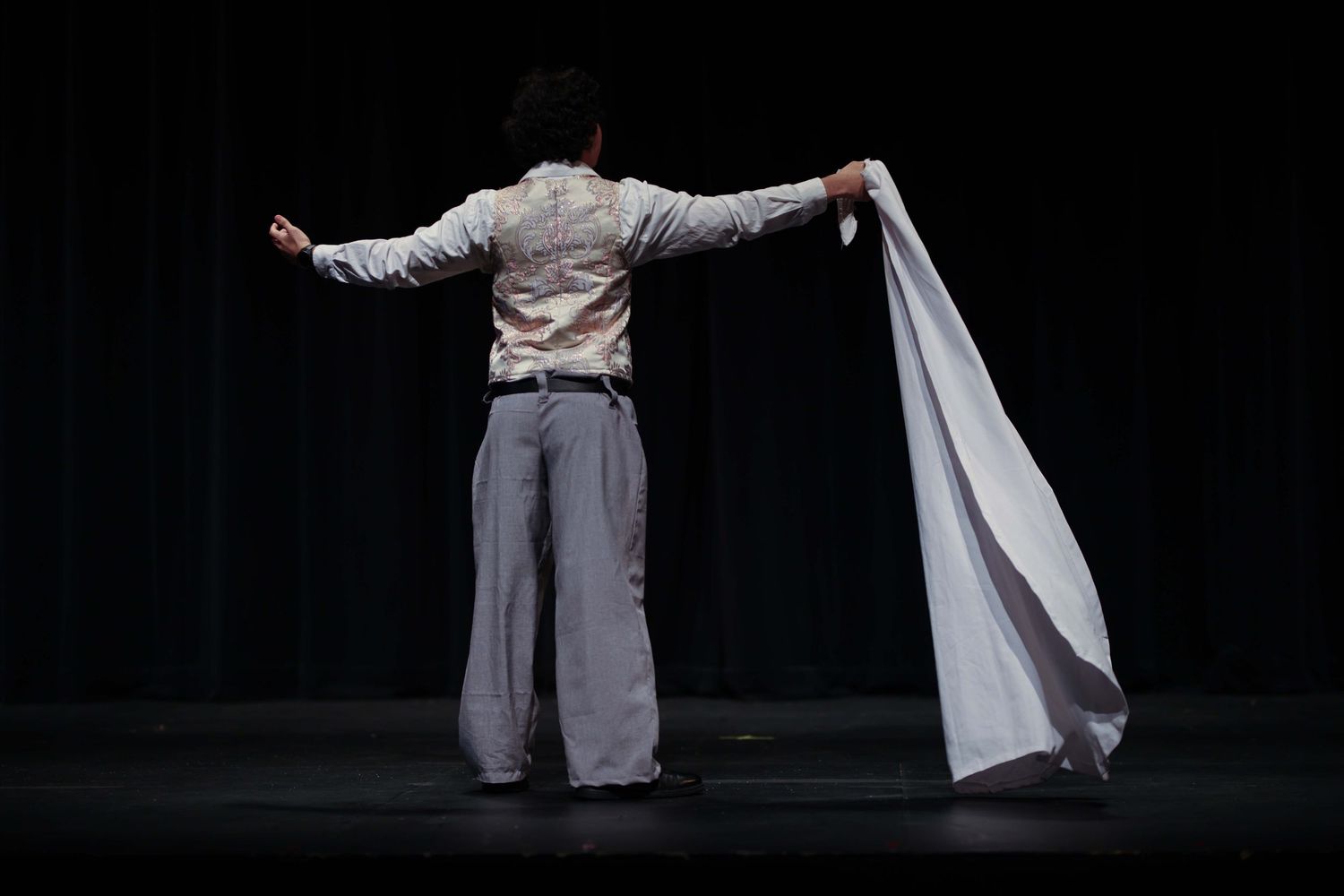 Dancer in white flowing costume performs dramatic movement sequence on dark stage.