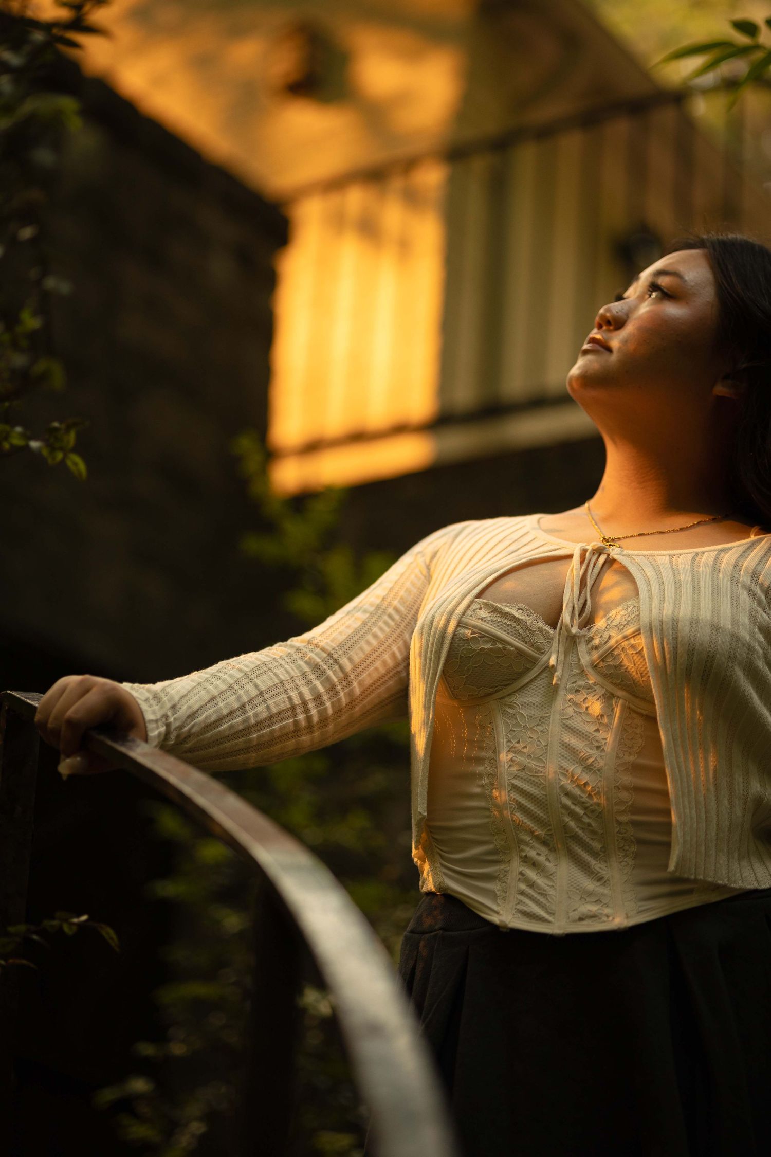 A person in a cream knit sweater and dark skirt poses against golden sunset light in an outdoor setting.