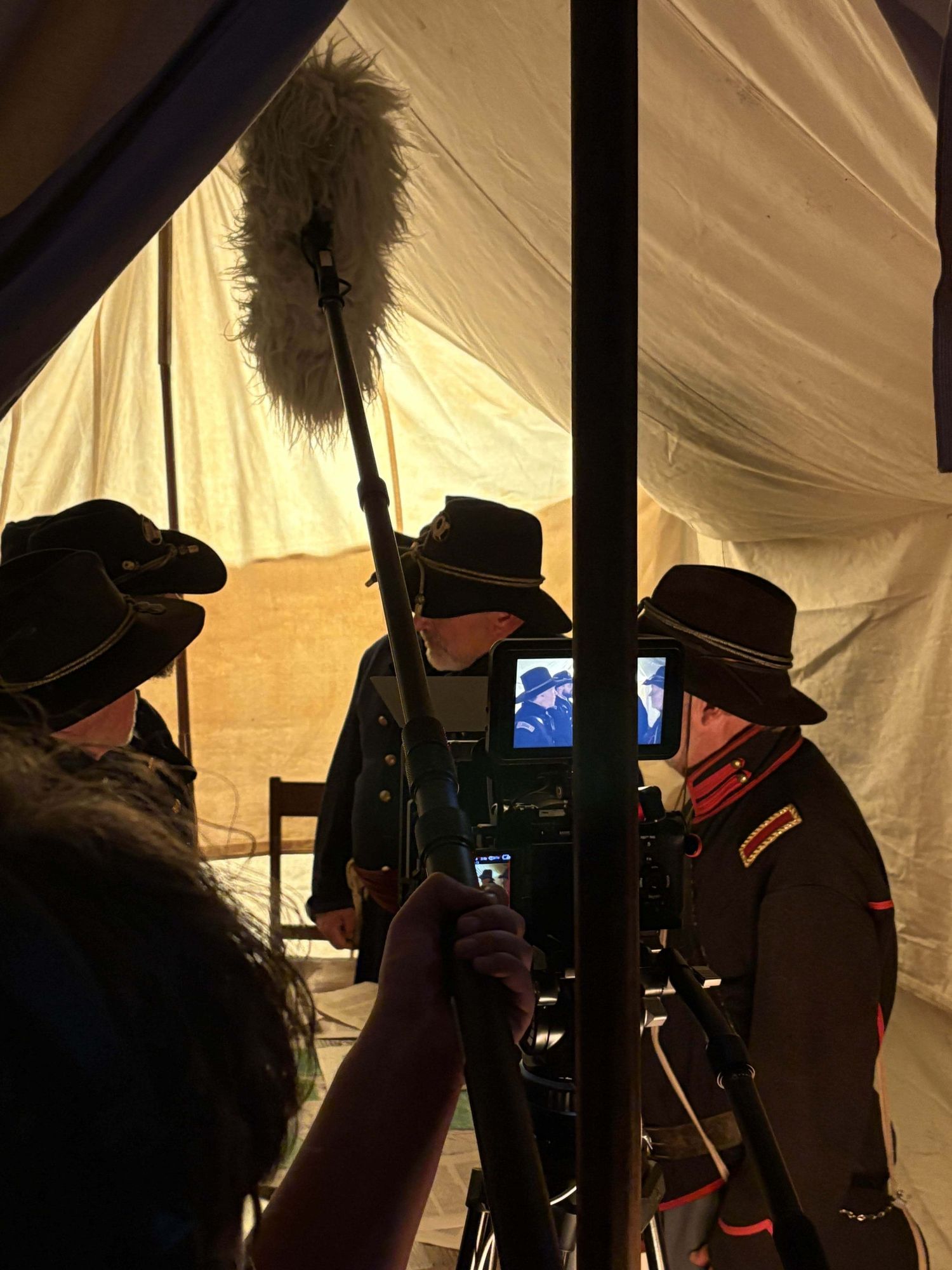 Film crew in cowboy hats working with equipment inside a dimly lit tent.