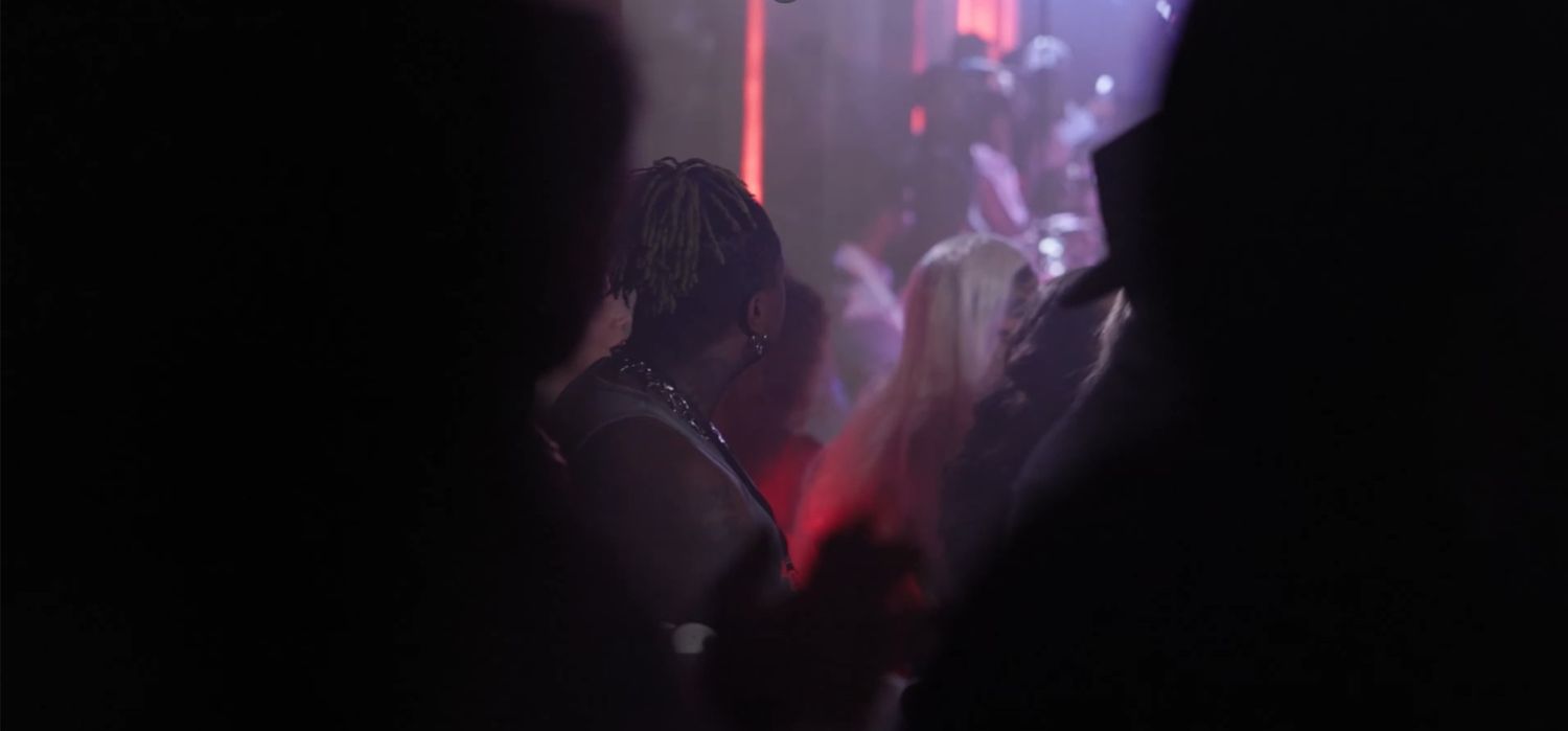 People dancing in a dimly lit nightclub with red and purple lights illuminating the dark dance floor.