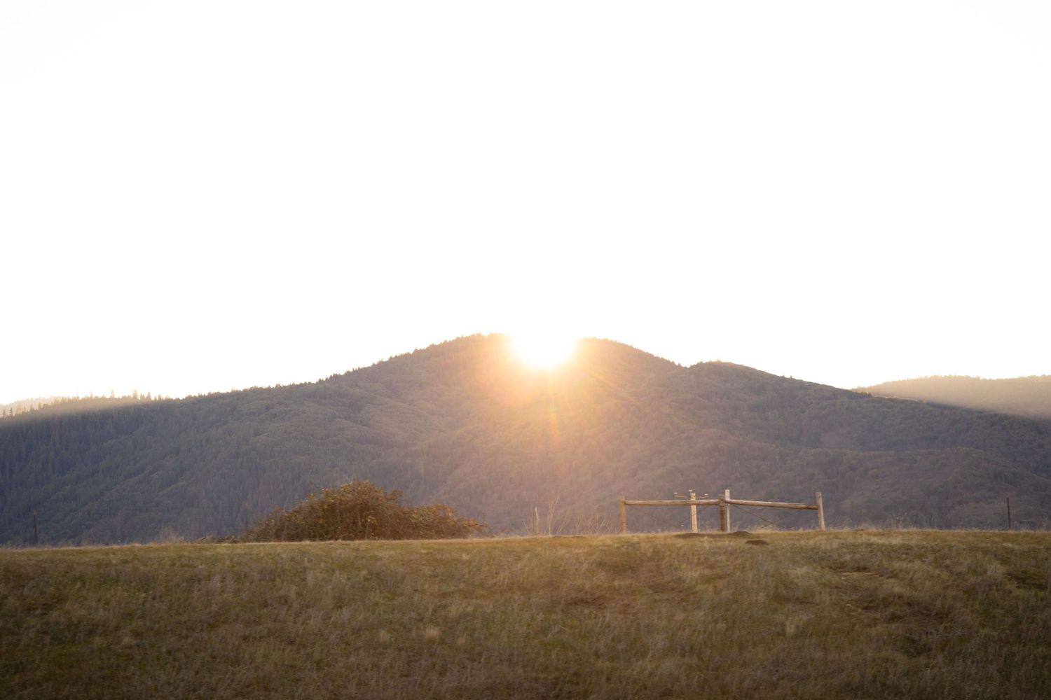 Golden sunburst peeks through clouds over rolling hills at sunset creating a dramatic mountain landscape.