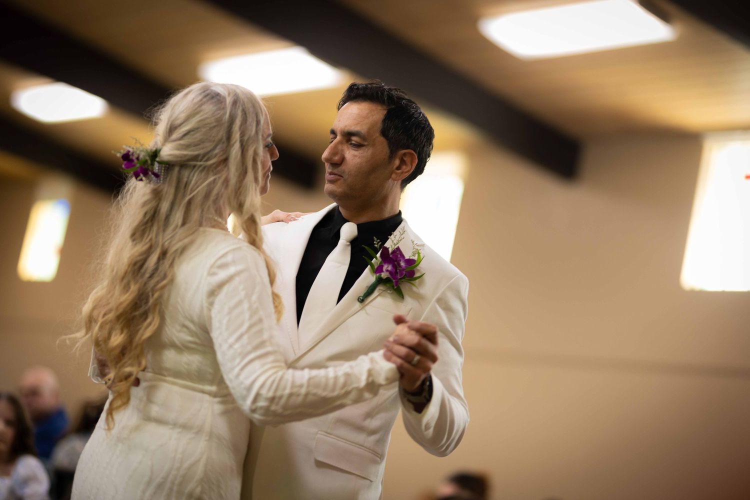 A couple in white outfits dance together during a ballroom dance lesson in a brightly lit studio.