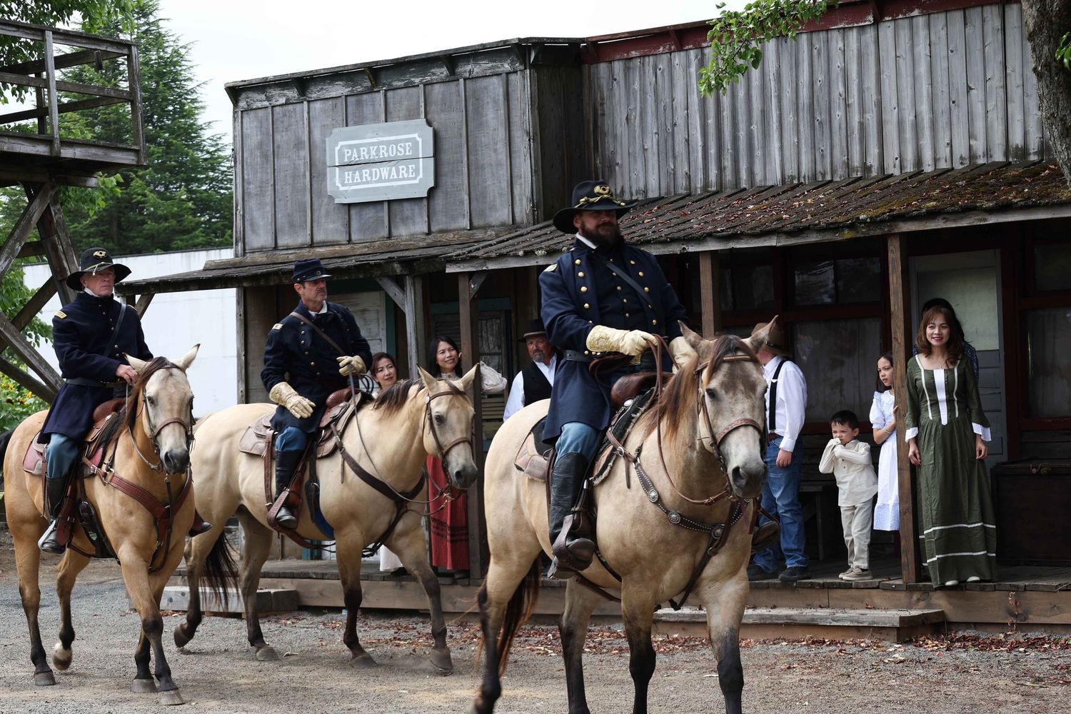 A line of horseback riders on brown and white horses wait outside a rustic wooden building.