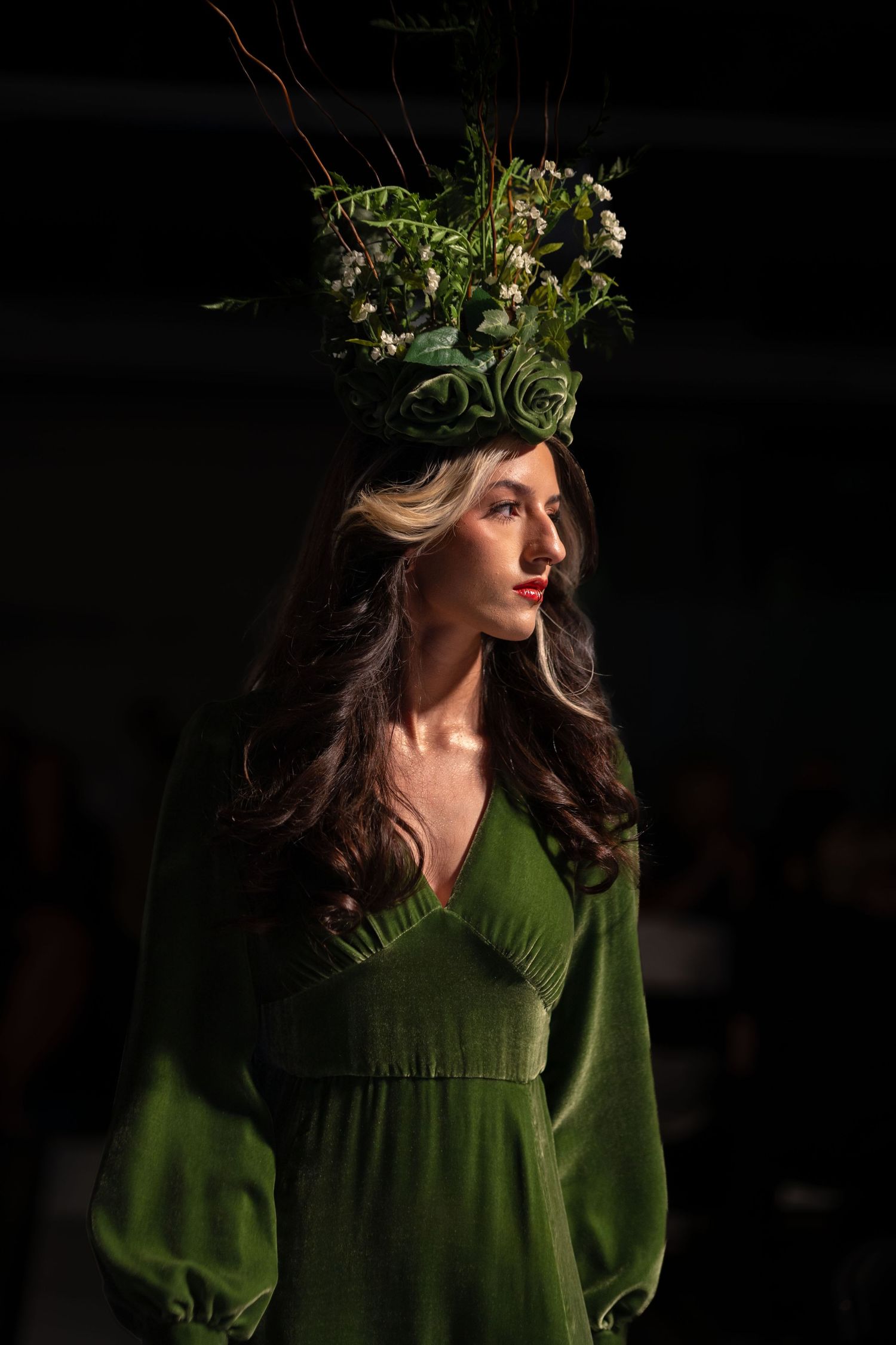 Model wearing ethereal green dress with botanical crown on dark runway.