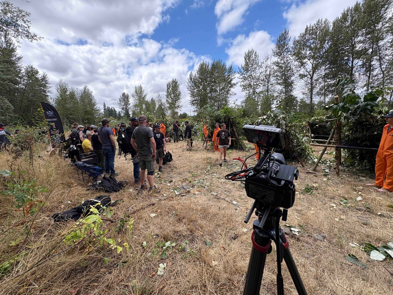 A panoramic view of people gathering on a rocky hillside during a daytime outdoor event in a forested area.