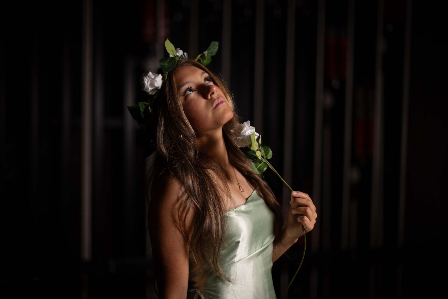 Bride in white dress poses with closed eyes and flowers in her hair against dark background.