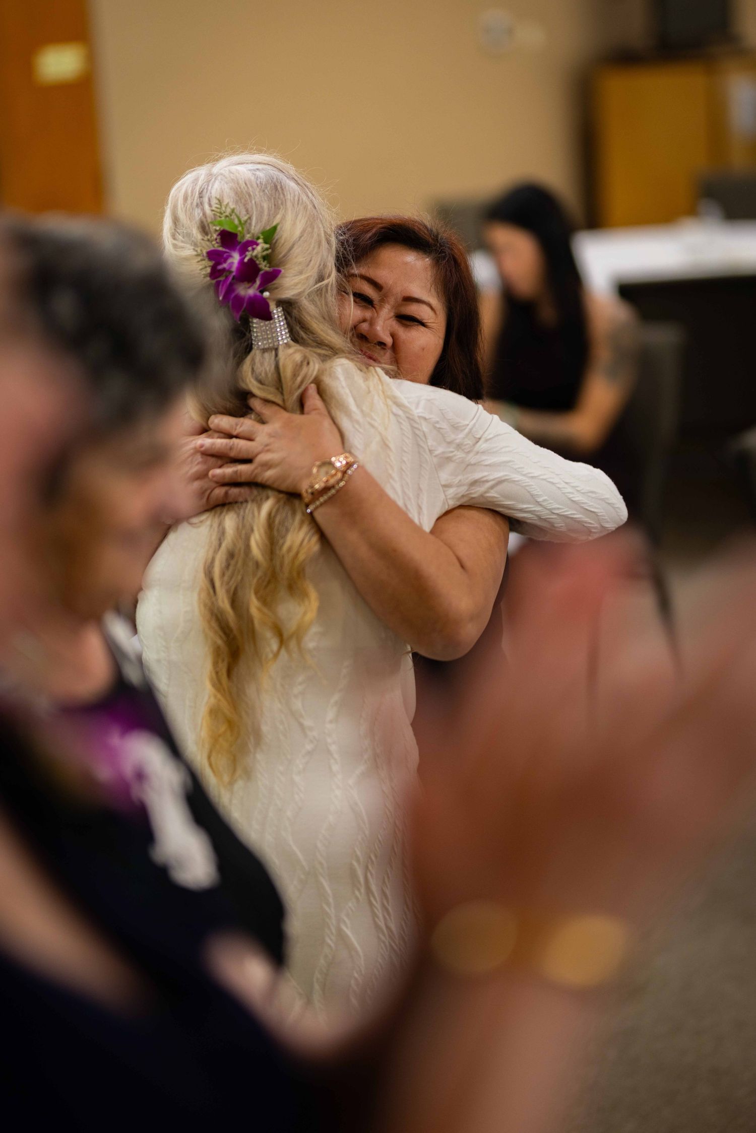 A tender embrace between two people dancing at a wedding reception, with a purple flower accent in view.