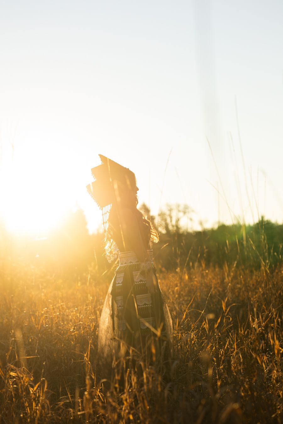 Silhouette of a woman standing in golden field at sunset, bathed in warm sunlight with tall grass surrounding her.