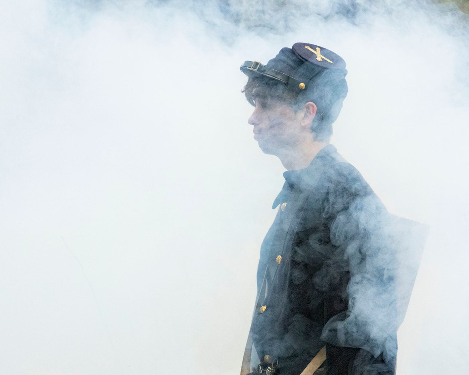 Civil War Union soldier reenactor in uniform and cap stands amid billowing smoke on a battlefield.