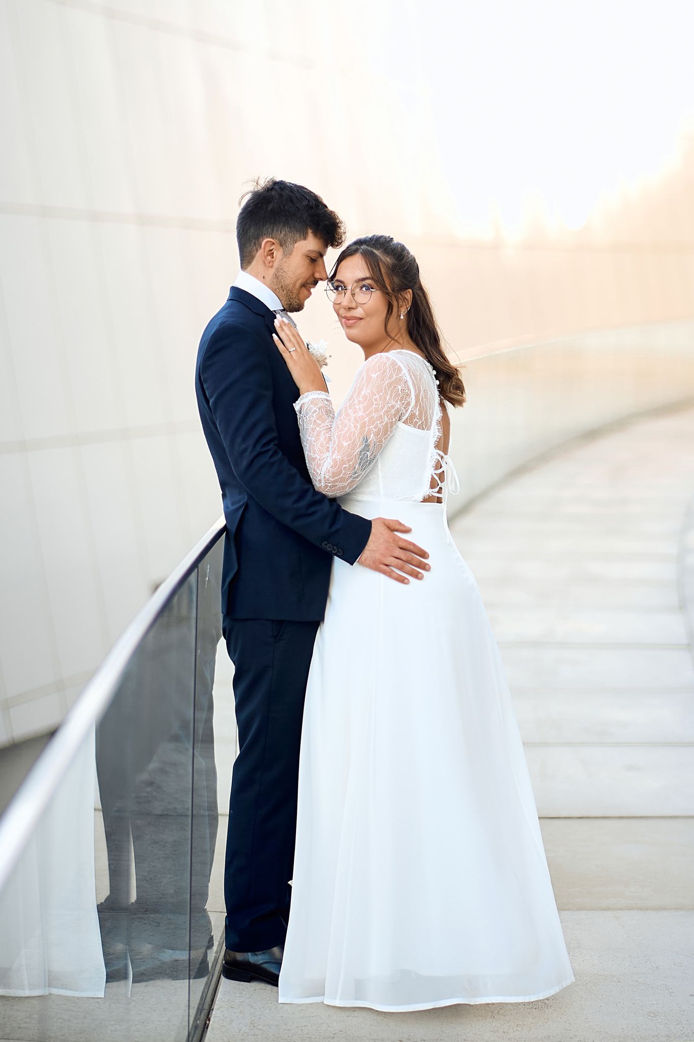 A gentle embrace captured against a bright white wall in wedding attire.